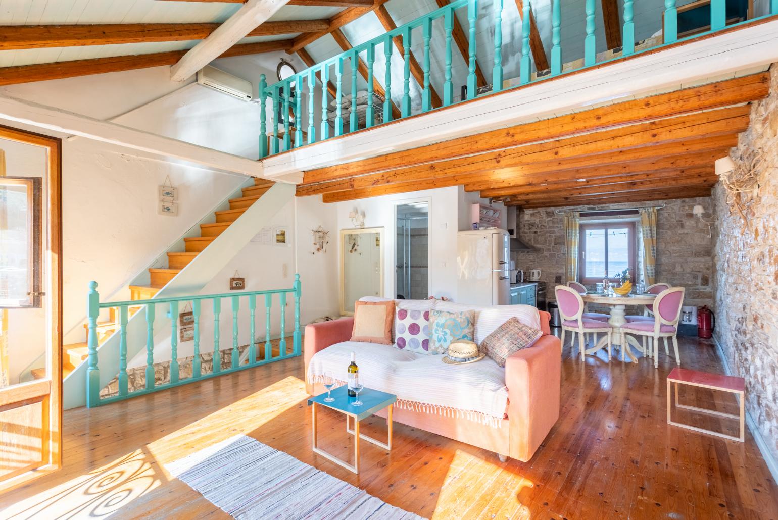 Open-plan living room with sofa-bed, dining area, kitchen, mezzanine, and sea views