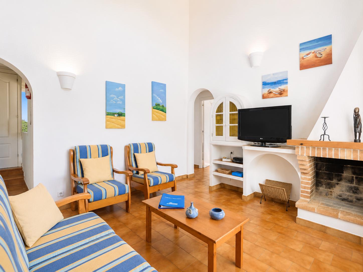 Open-plan living room with sofas, dining area, kitchen, ornamental fireplace, A/C, WiFi internet, and satellite TV