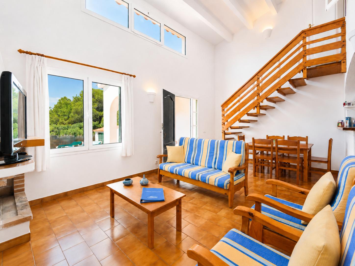Open-plan living room with sofas, dining area, kitchen, ornamental fireplace, A/C, WiFi internet, and satellite TV