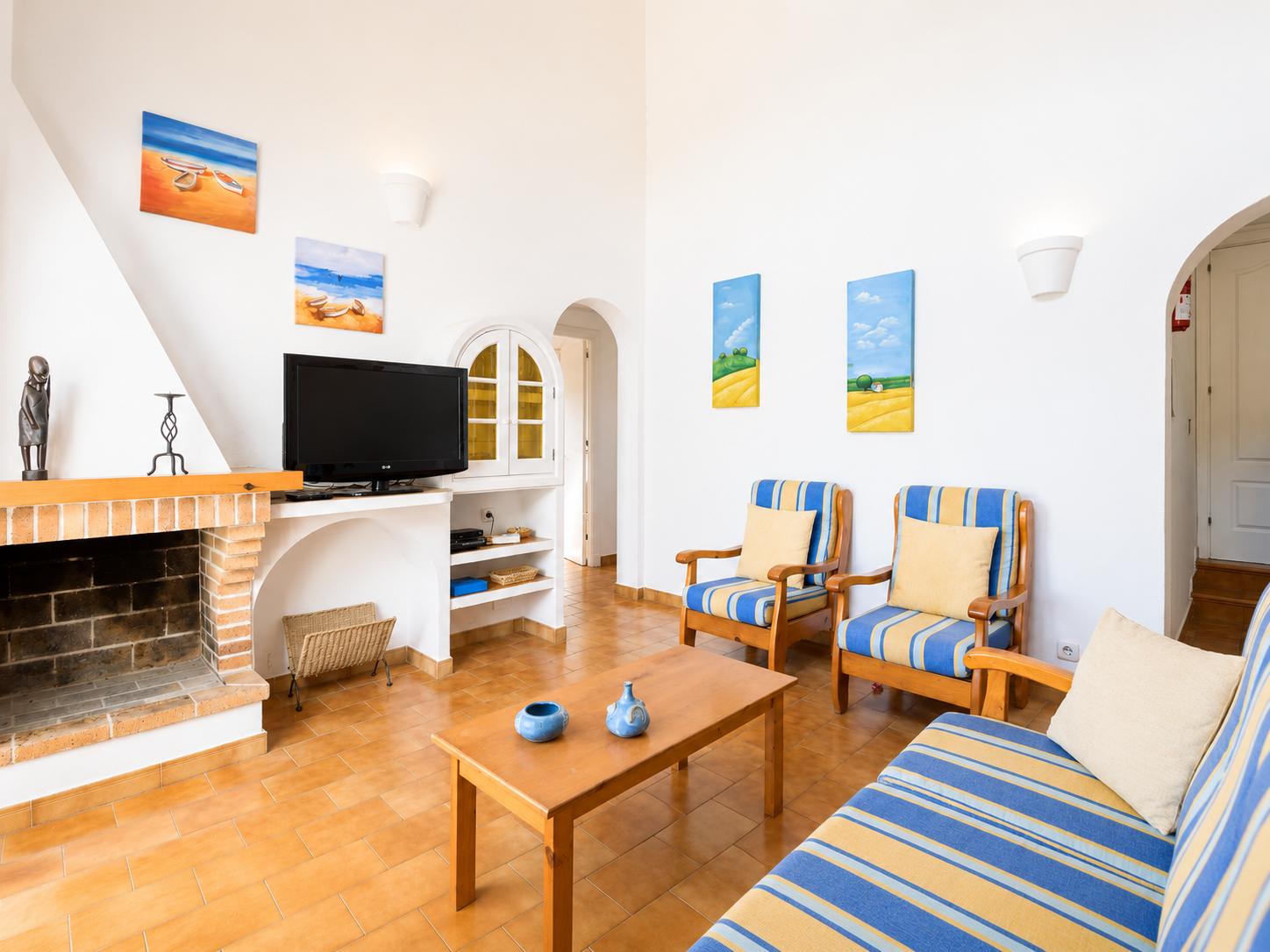 Open-plan living room with sofas, dining area, kitchen, ornamental fireplace, A/C, WiFi internet, and satellite TV