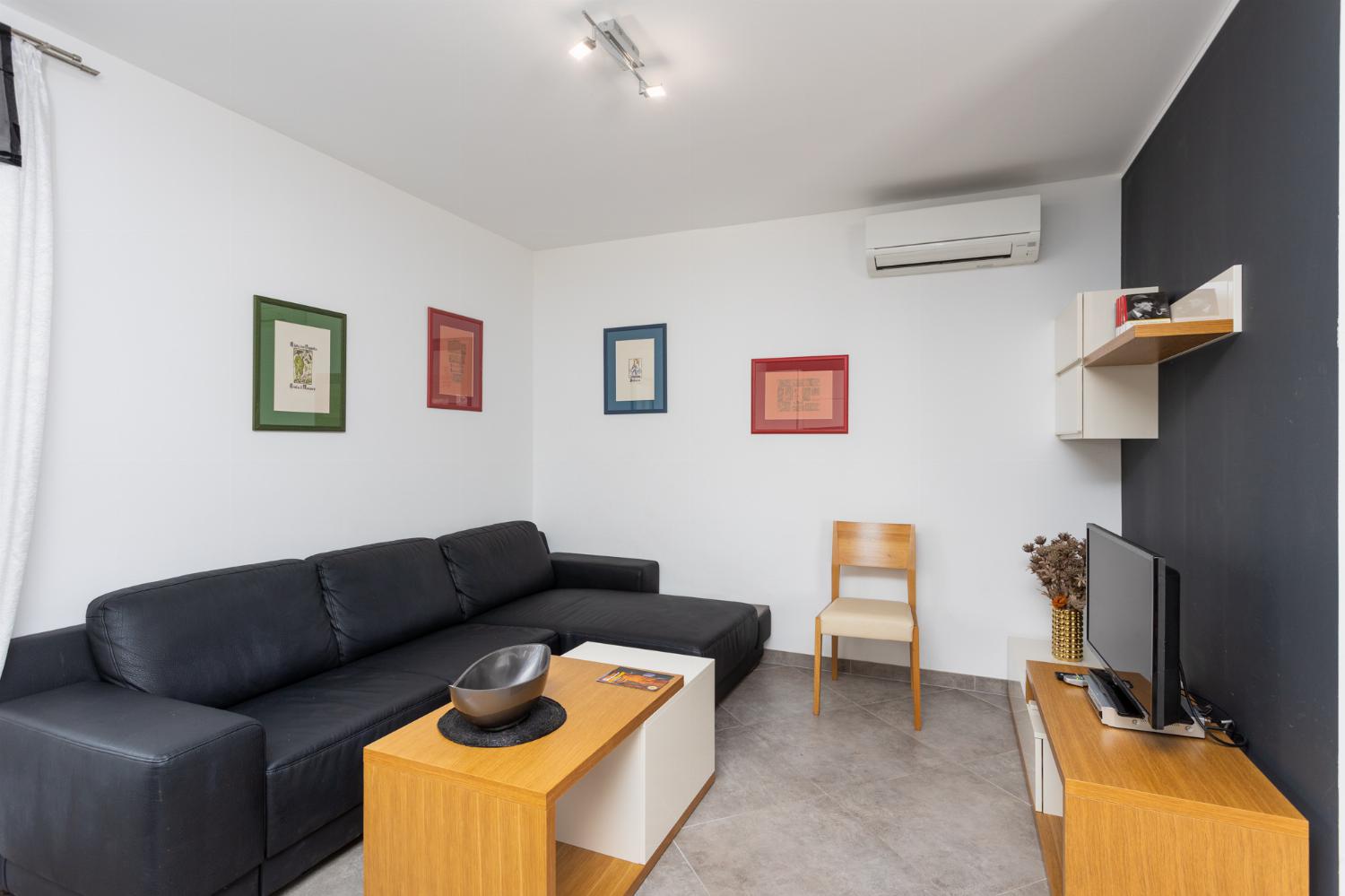 Open-plan living room with sofa, dining area, kitchen, A/C, WiFi internet, and satellite TV