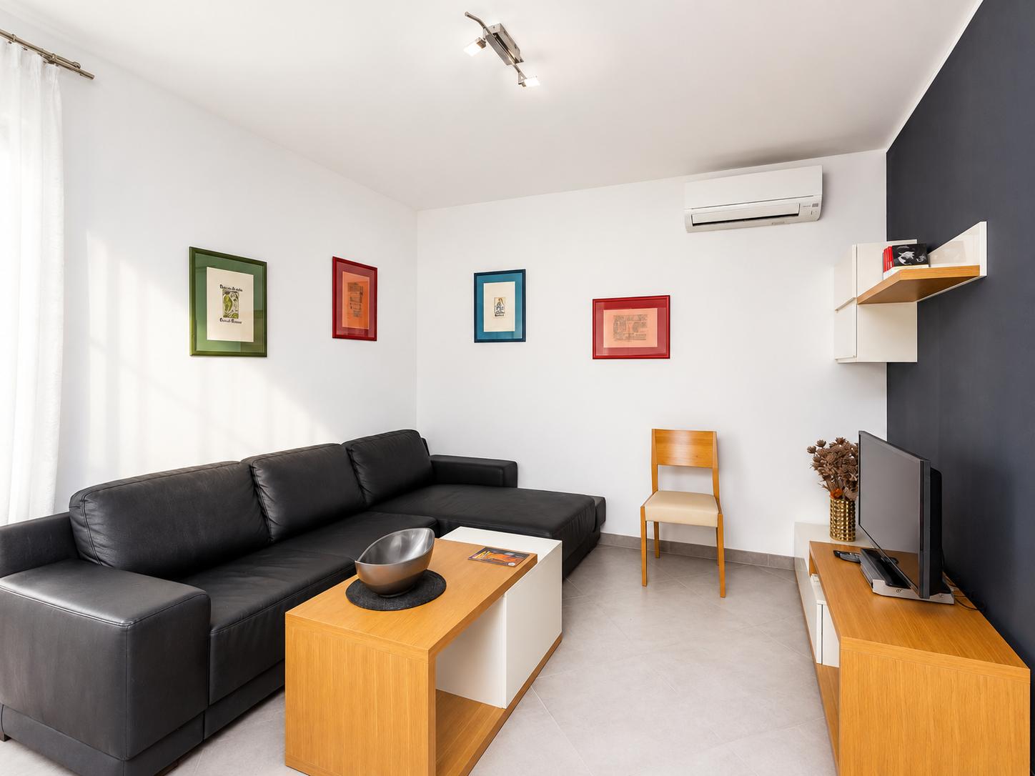 Open-plan living room with sofa, dining area, kitchen, A/C, WiFi internet, and satellite TV