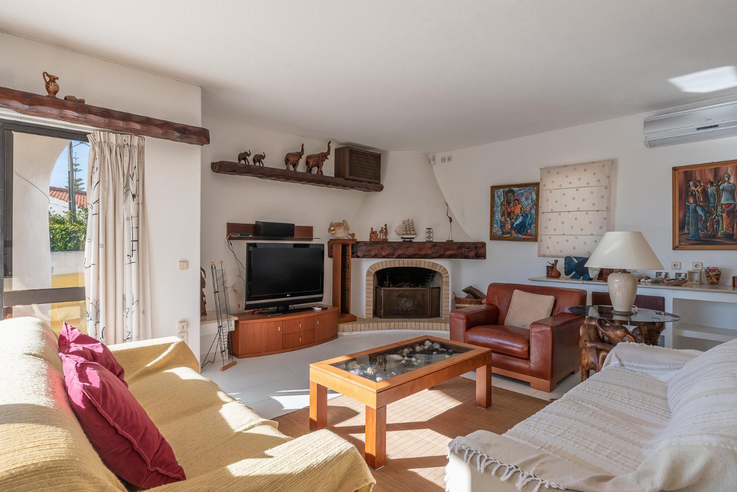 Open-plan living room with sofas, ornamental fireplace, dining area, kitchen, A/C, WiFi internet, satellite TV, DVD player, and pool terrace access
