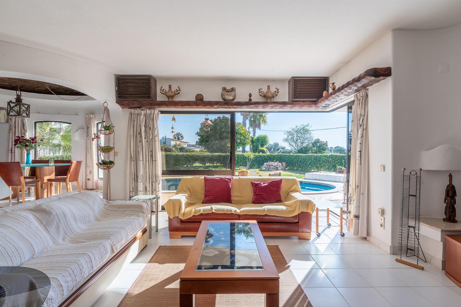 Open-plan living room with sofas, ornamental fireplace, dining area, kitchen, A/C, WiFi internet, satellite TV, DVD player, and pool terrace access