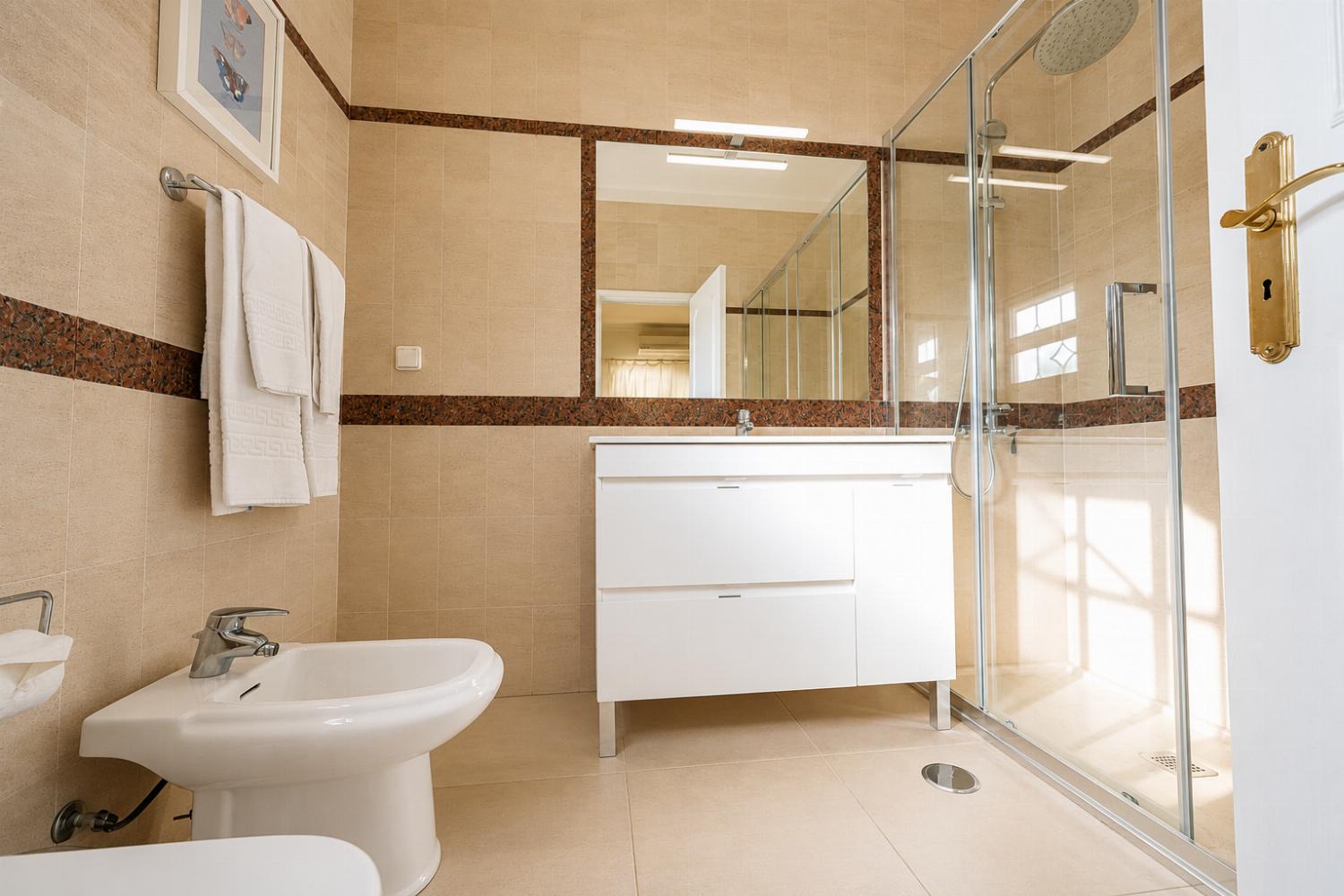 Well-lit modern bathroom with a white vanity setup, bidet, and glass walk-in shower.