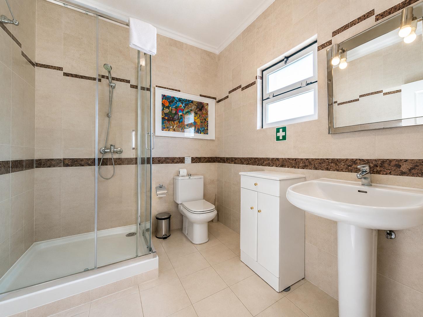 Tiled bathroom featuring a glass shower stall, pedestal sink, and small vanity cabinet.