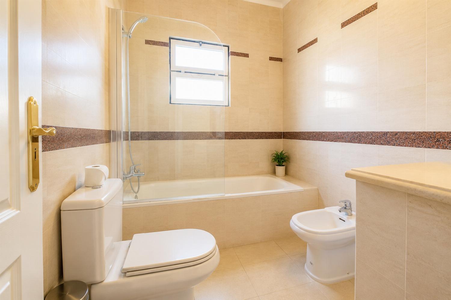Tiled bathroom featuring a combination bathtub and shower with a glass splash panel, toilet, and bidet.