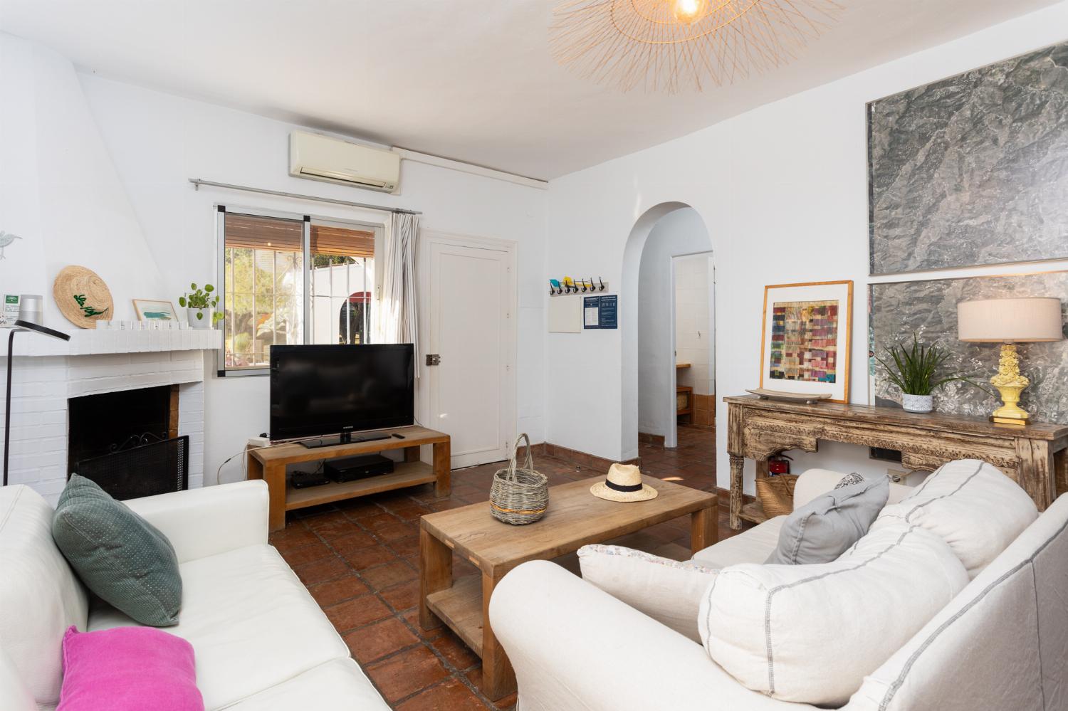 Open-plan living room with sofas, dining area, kitchen, ornamental fireplace, A/C, WiFi internet, and satellite TV