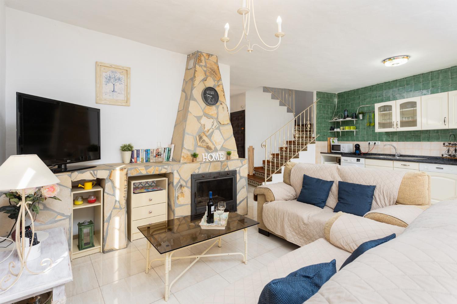 Open-plan living room with sofas, dining area, kitchen, ornamental fireplace, A/C, WiFi internet, and satellite TV