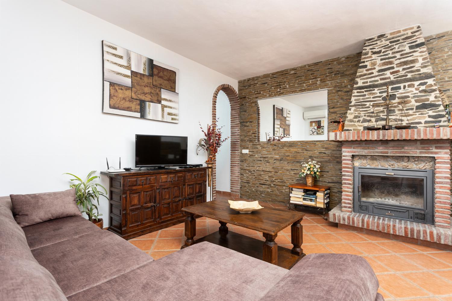 Open-plan living room with sofa, dining area, kitchen, ornamental fireplace, A/C, WiFi internet, and satellite TV