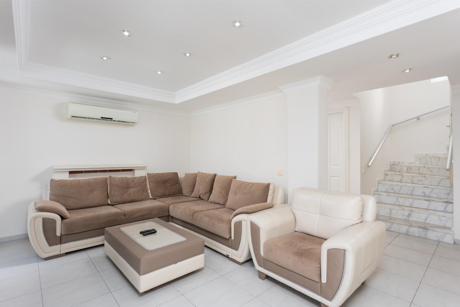 Open-plan living room with sofas, dining area, kitchen, ornamental fireplace, A/C, WiFi internet, and satellite TV