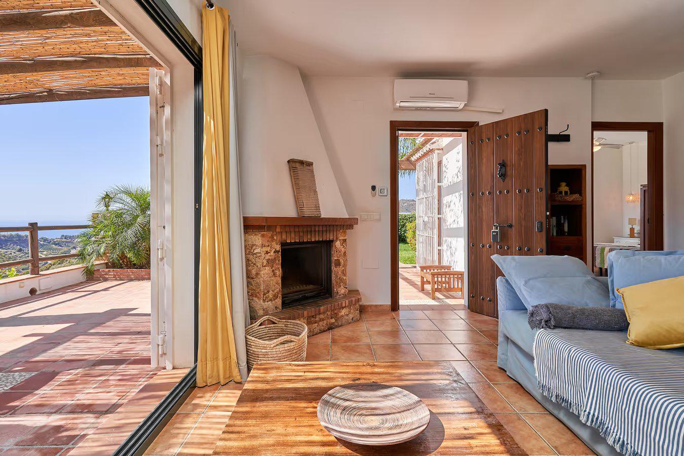 Open-plan living room with sofas, dining area, kitchen, ornamental fireplace, A/C, WiFi internet, satellite TV, and patio doors