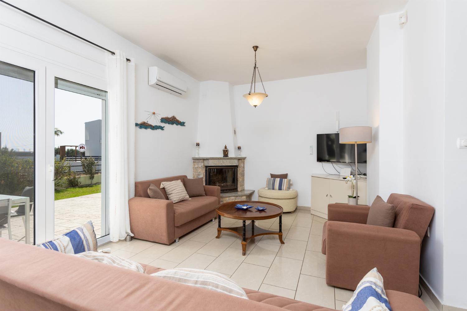 Open-plan living room with sofas, dining area, kitchen, ornamental fireplace, A/C, WiFi internet, and satellite TV