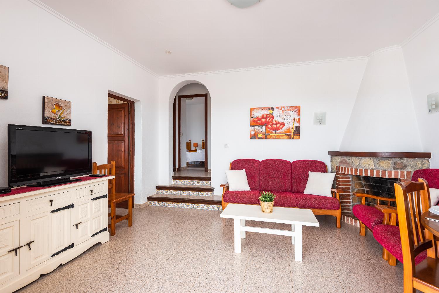 Open-plan living room with sofas, ornamental fireplace, dining area, kitchen, A/C, WiFi internet, satellite TV, DVD player, and pool terrace access