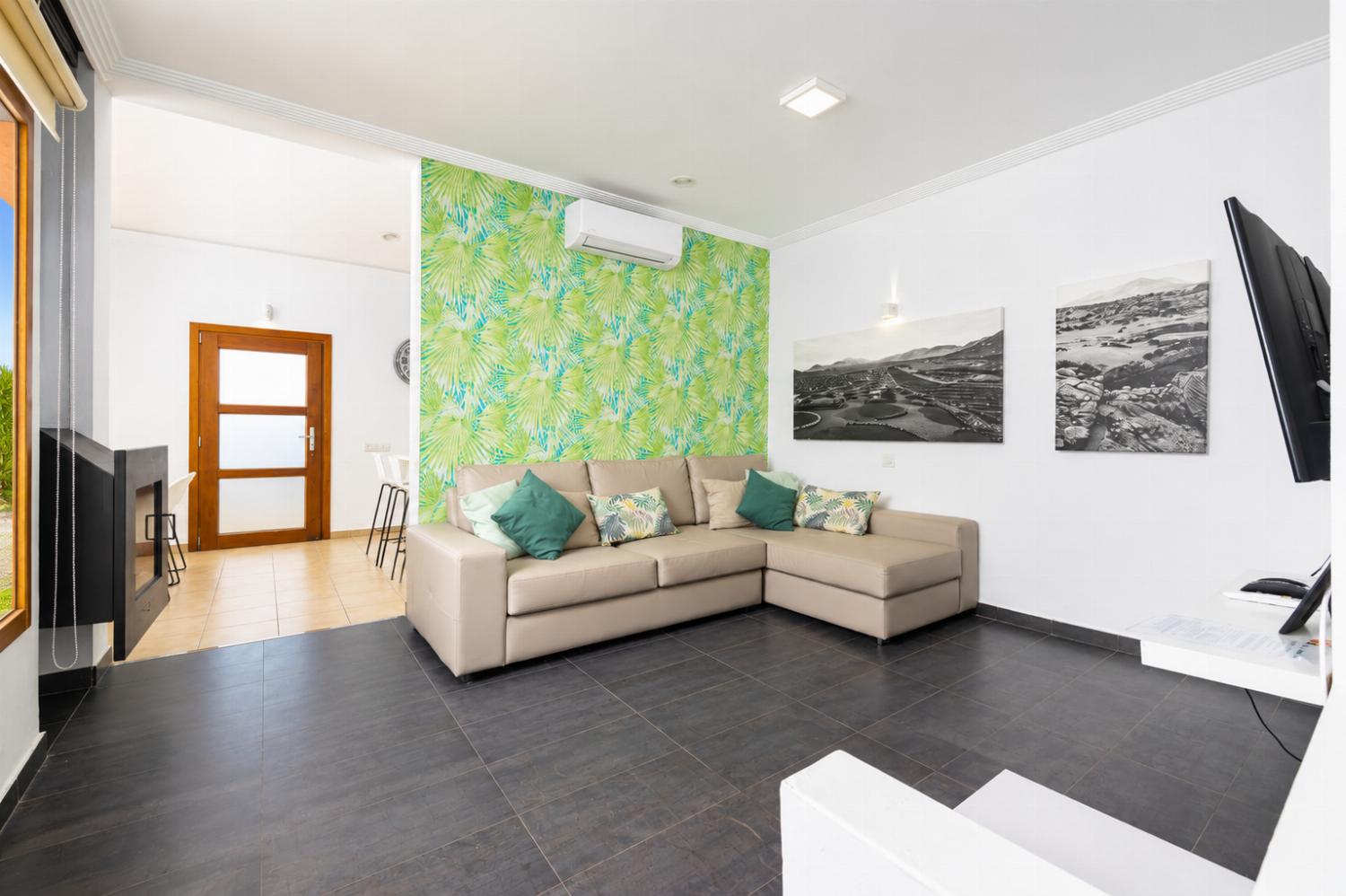Open-plan living room with sofa, dining area, kitchen, ornamental fireplace, A/C, WiFi internet, and satellite TV