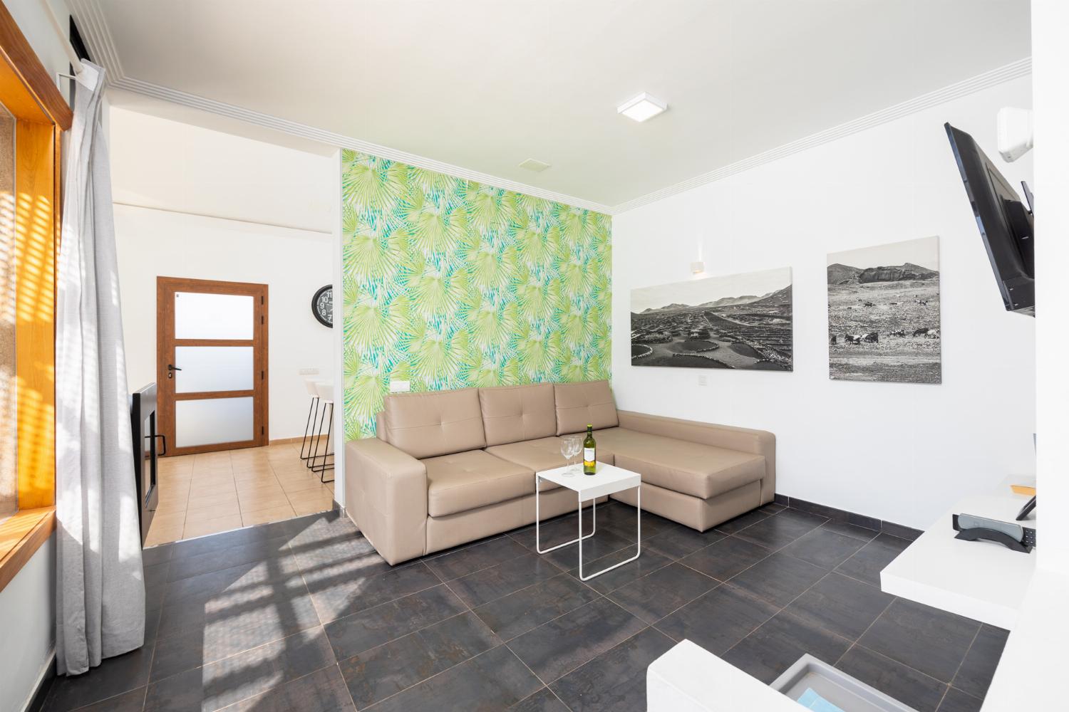 Open-plan living room with sofa, dining area, kitchen, ornamental fireplace, A/C, WiFi internet, and satellite TV