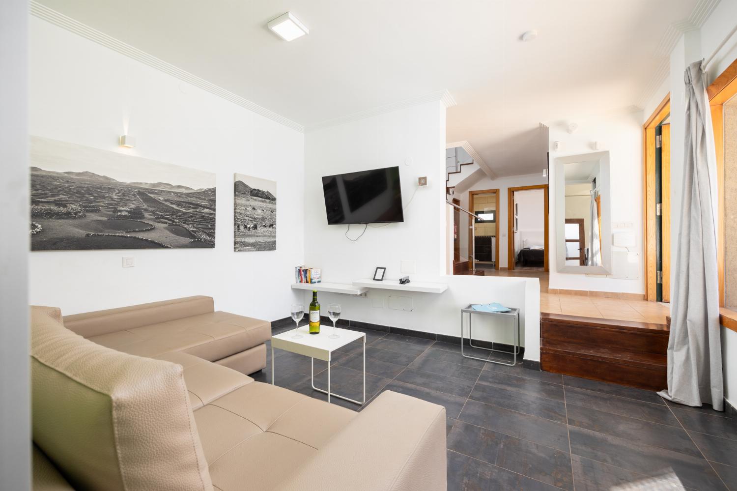 Open-plan living room with sofa, dining area, kitchen, ornamental fireplace, A/C, WiFi internet, and satellite TV