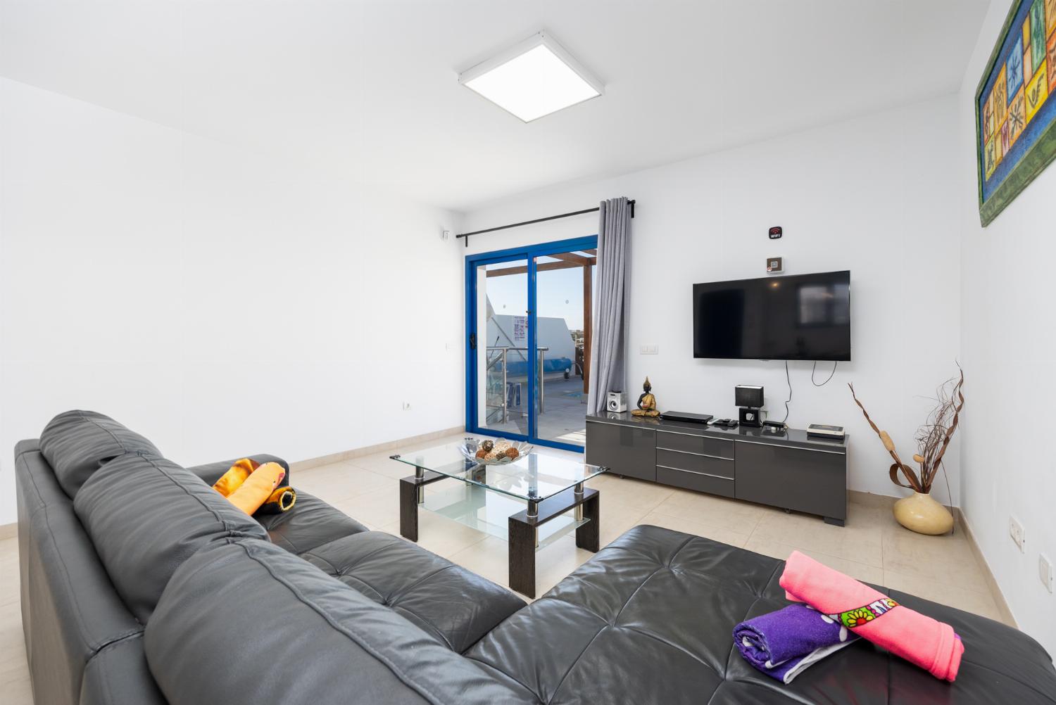 Open-plan living room with sofa, dining area, kitchen, A/C, WiFi internet, and satellite TV