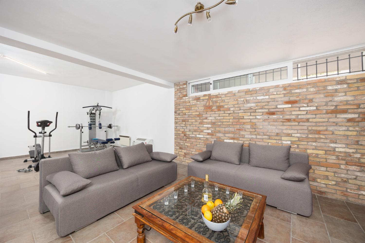 Open-plan living room on ground floor with sofas, dining area, bar area, ornamental fireplace, gym area, WiFi internet, and satellite TV