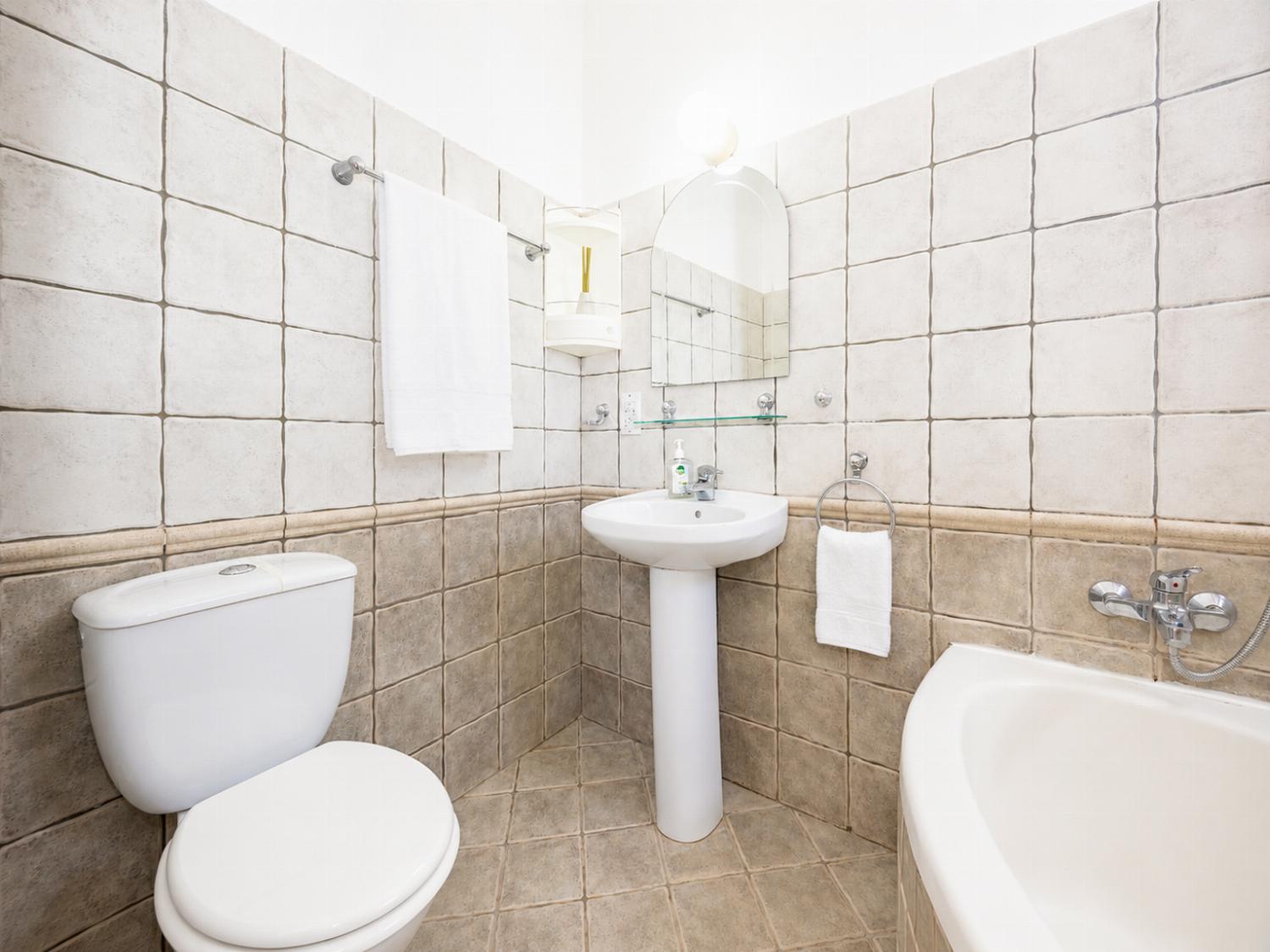 A bright, tiled villa bathroom featuring a built-in bathtub, a pedestal sink, a toilet, and vibrant pink accent towels.