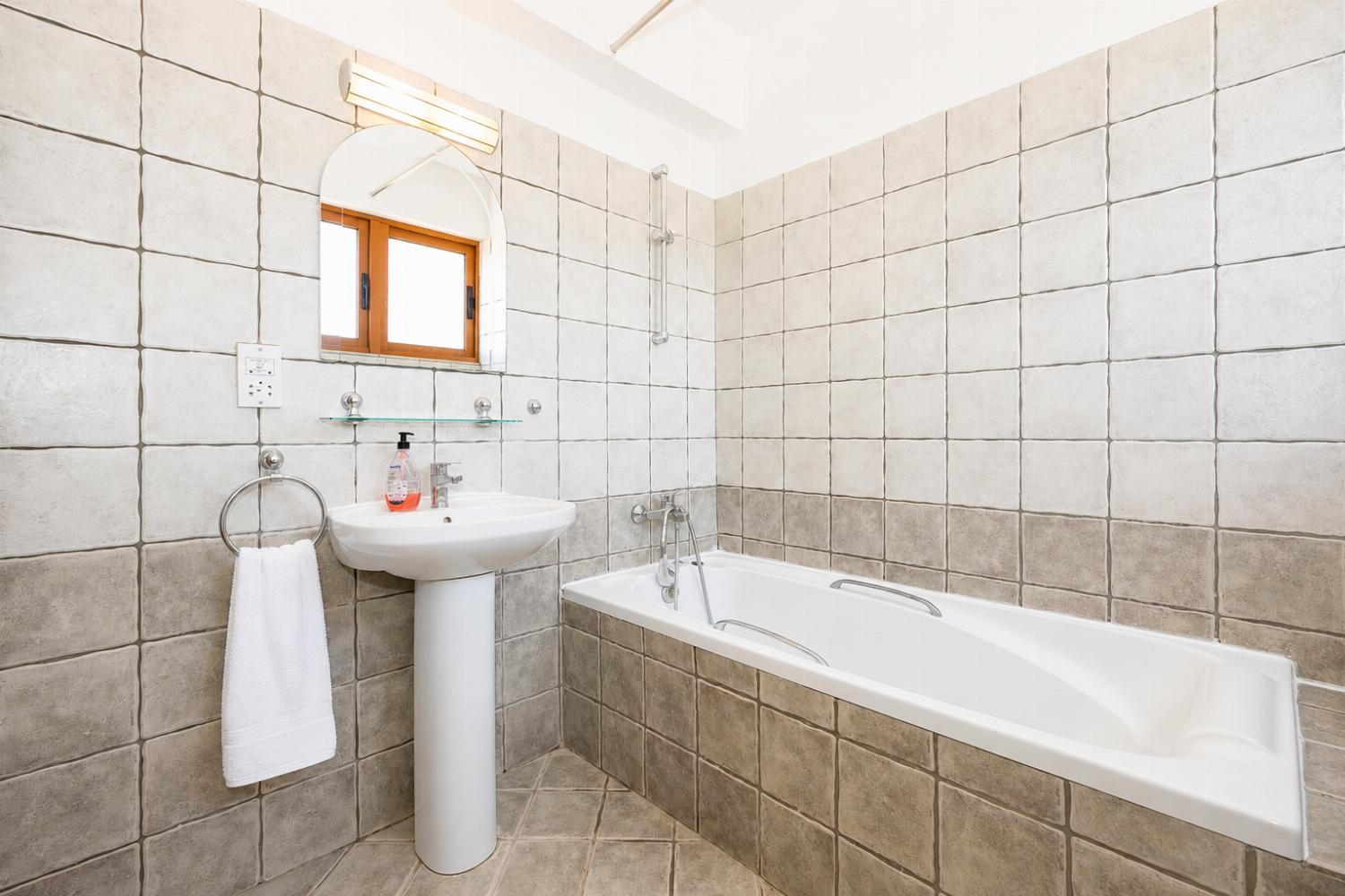 An interior view of an alternate bathroom within the property, utilizing a similar tile scheme but configured with a full bathtub setup.
