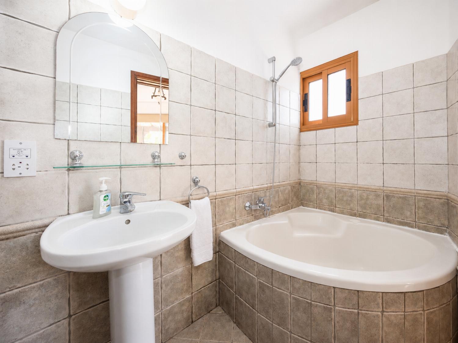 A bright, fully tiled bathroom featuring a corner shower enclosure, a pedestal sink with an arched mirror, and vibrant pink accents.