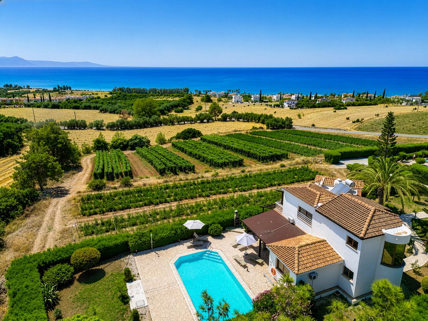 An expansive, high-angle aerial view of the property, showcasing the villa's private pool area and its integration into the surrounding agricultural landscape and coastline.