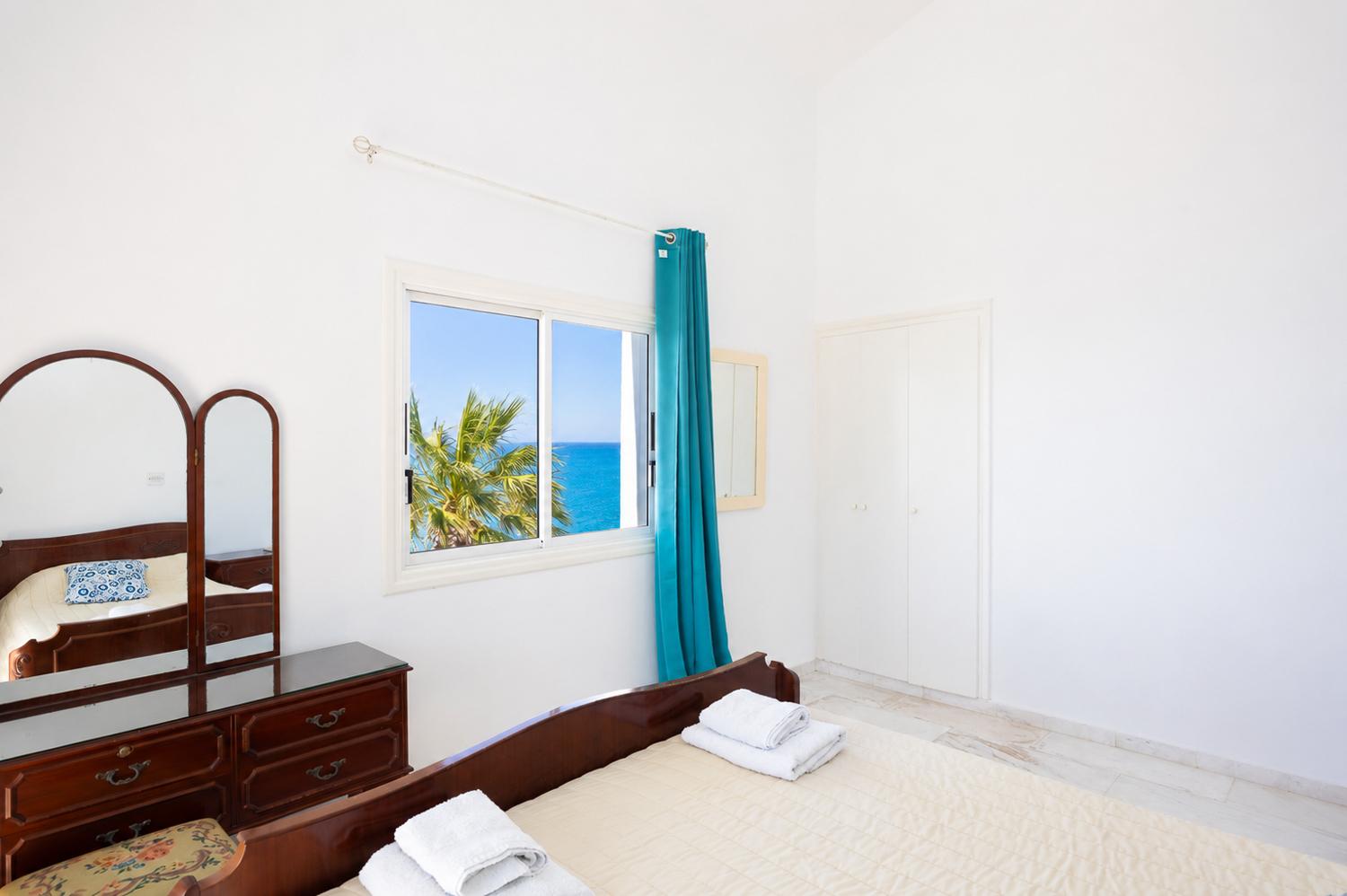 Bright bedroom with classic wooden furniture, turquoise curtains, and lovely sea views.