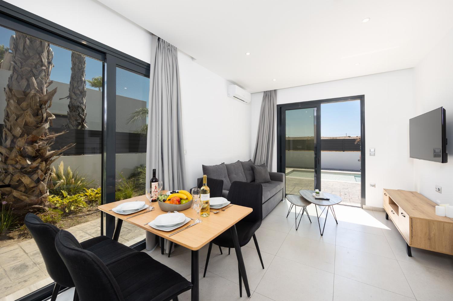 Open-plan living room with sofa, dining area, kitchen, A/C, WiFi internet, and satellite TV