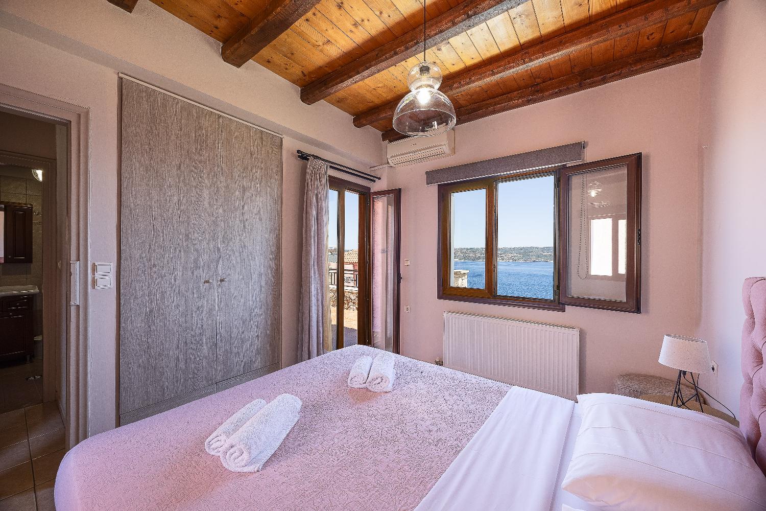 An alternate bedroom interior within the villa, showcasing a softer color scheme and expansive coastal views.