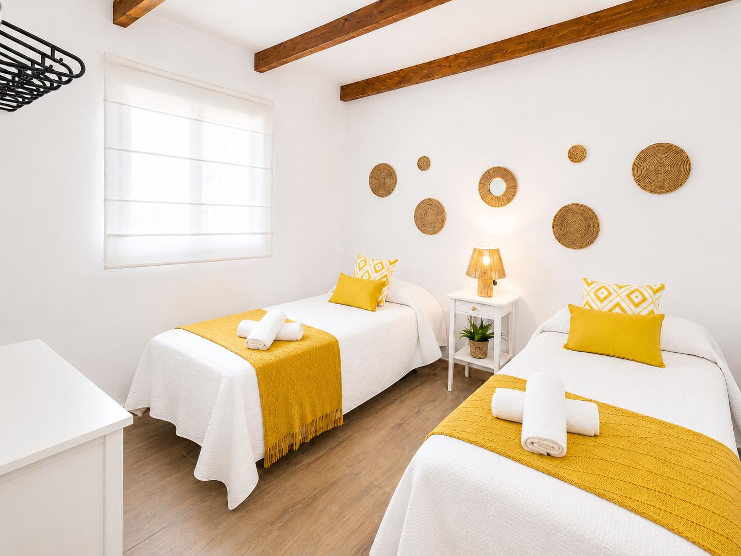 Bright twin bedroom with yellow accents, wooden beams, and warm natural decor.