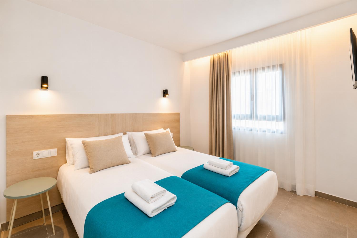 Bright twin bedroom with soft neutral tones, and warm natural light.