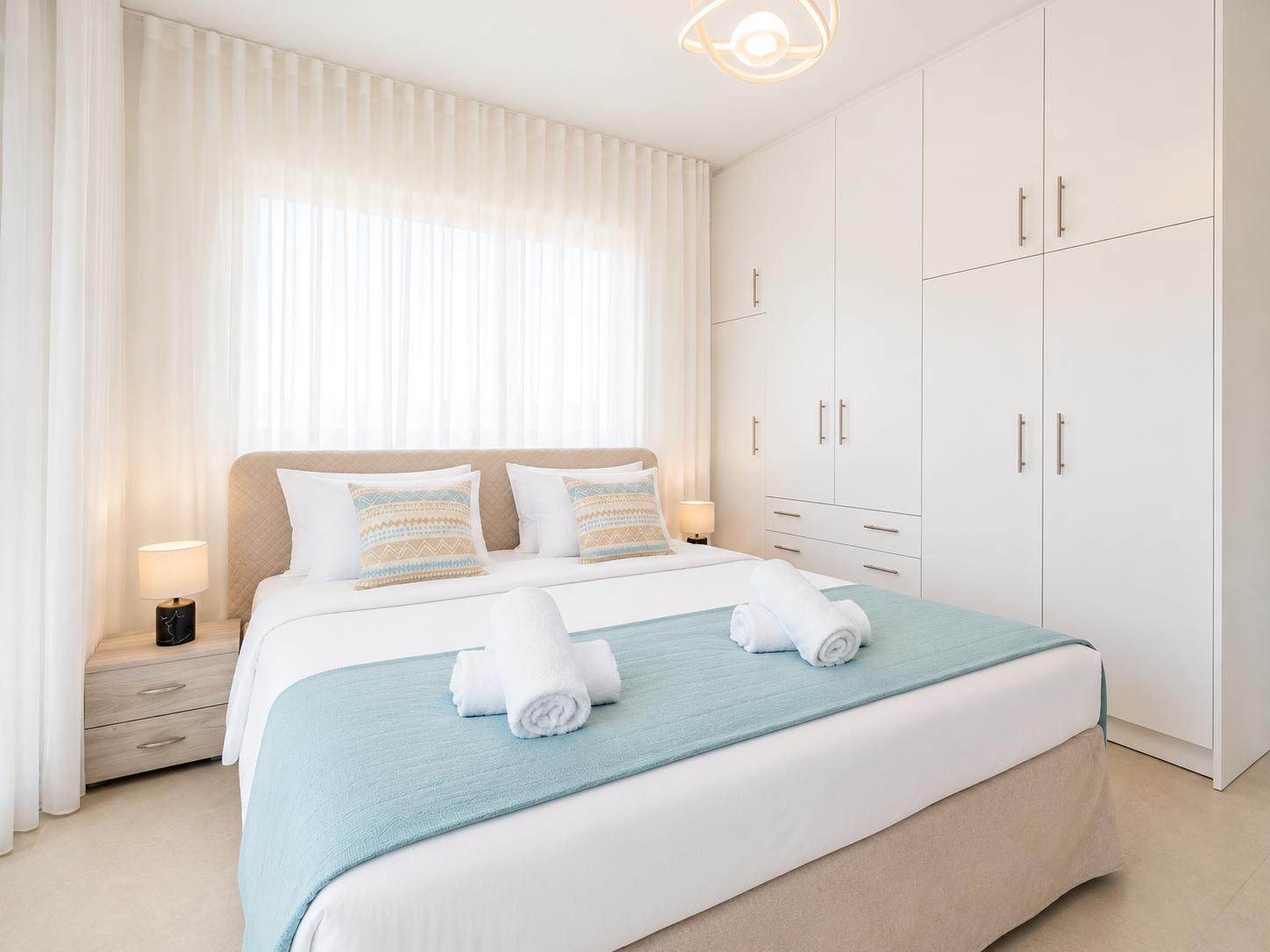 Bright double bedroom with soft blue accents, white wardrobes, and elegant modern decor.