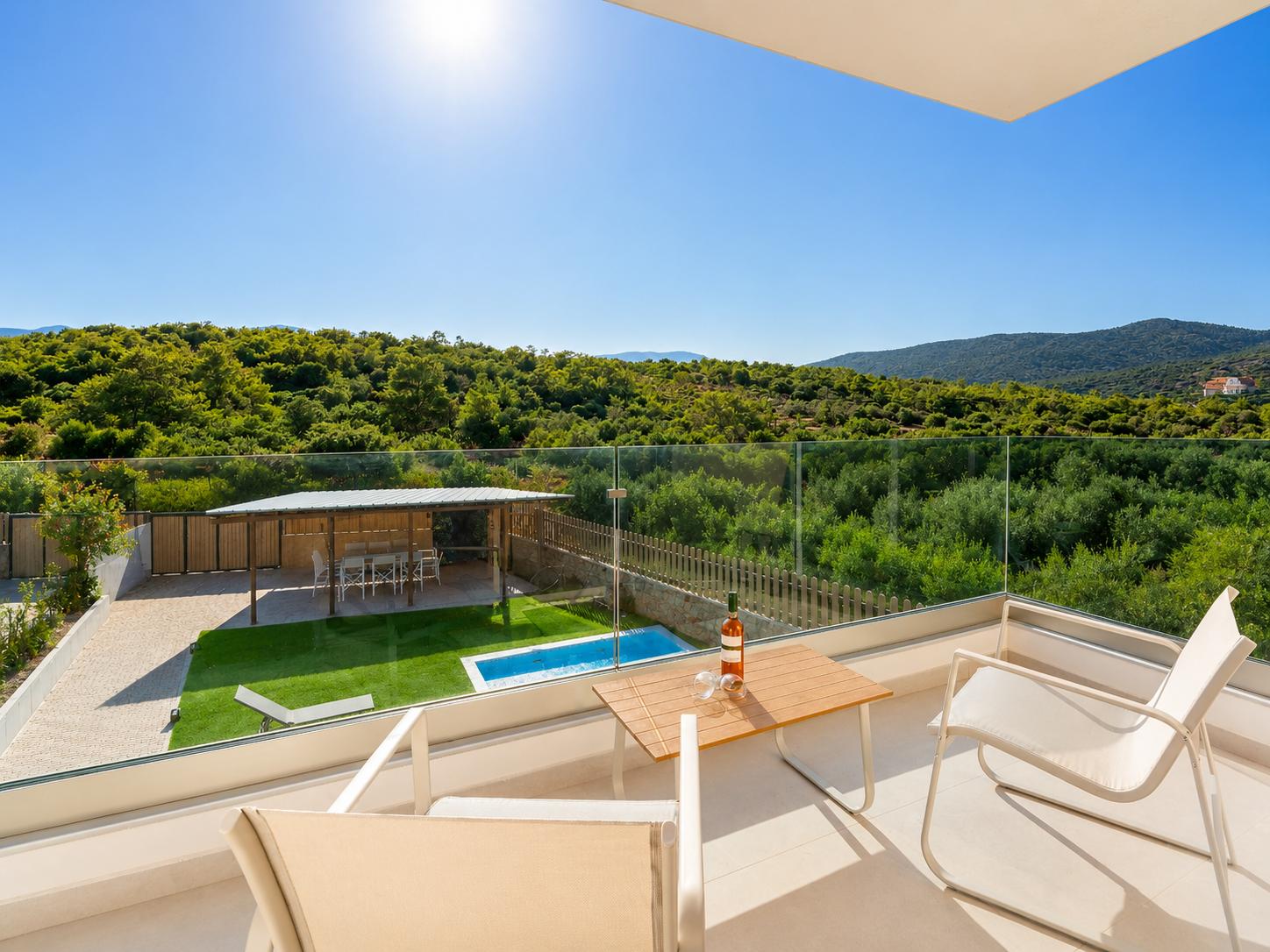 Sunny private balcony with comfortable seating, glass railings, and peaceful forest views.