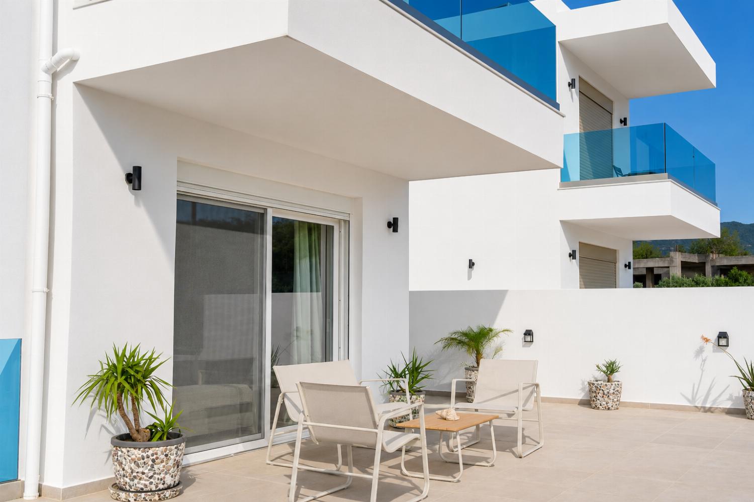 Sunny private terrace with modern seating, potted greenery, and sleek glass balconies.