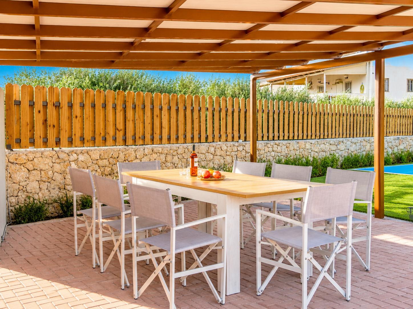 Shaded outdoor dining area with a wooden pergola, modern seating, and a sunny garden setting.