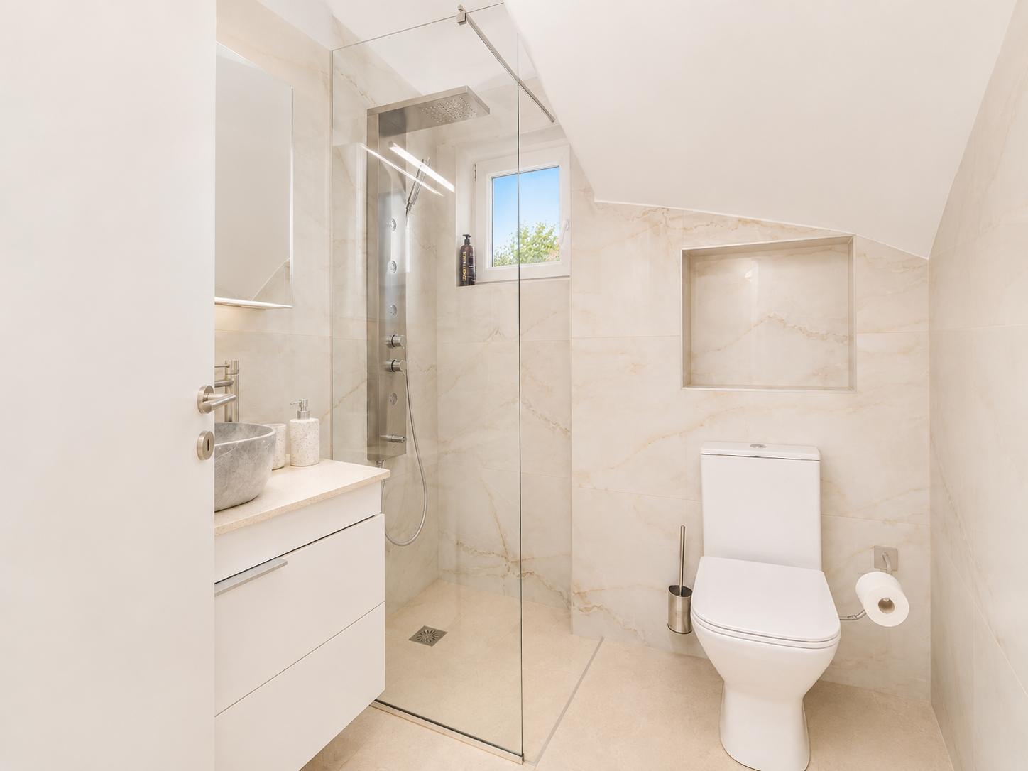 Modern bathroom with a walk-in glass shower, white vanity, and bright marble-style finishes.