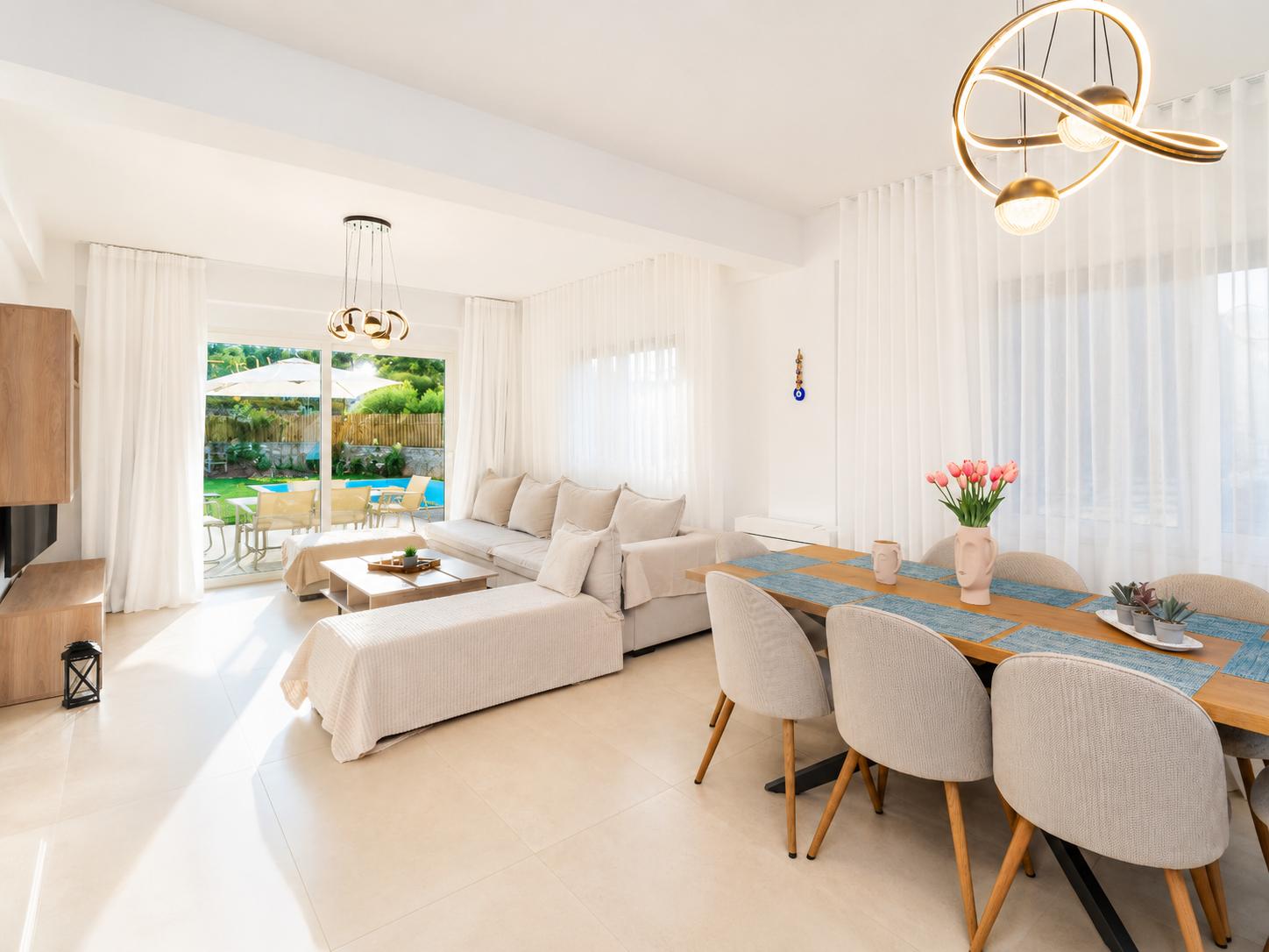 Bright open-plan living and dining area with elegant white decor, modern lighting, and direct access to the private pool terrace.