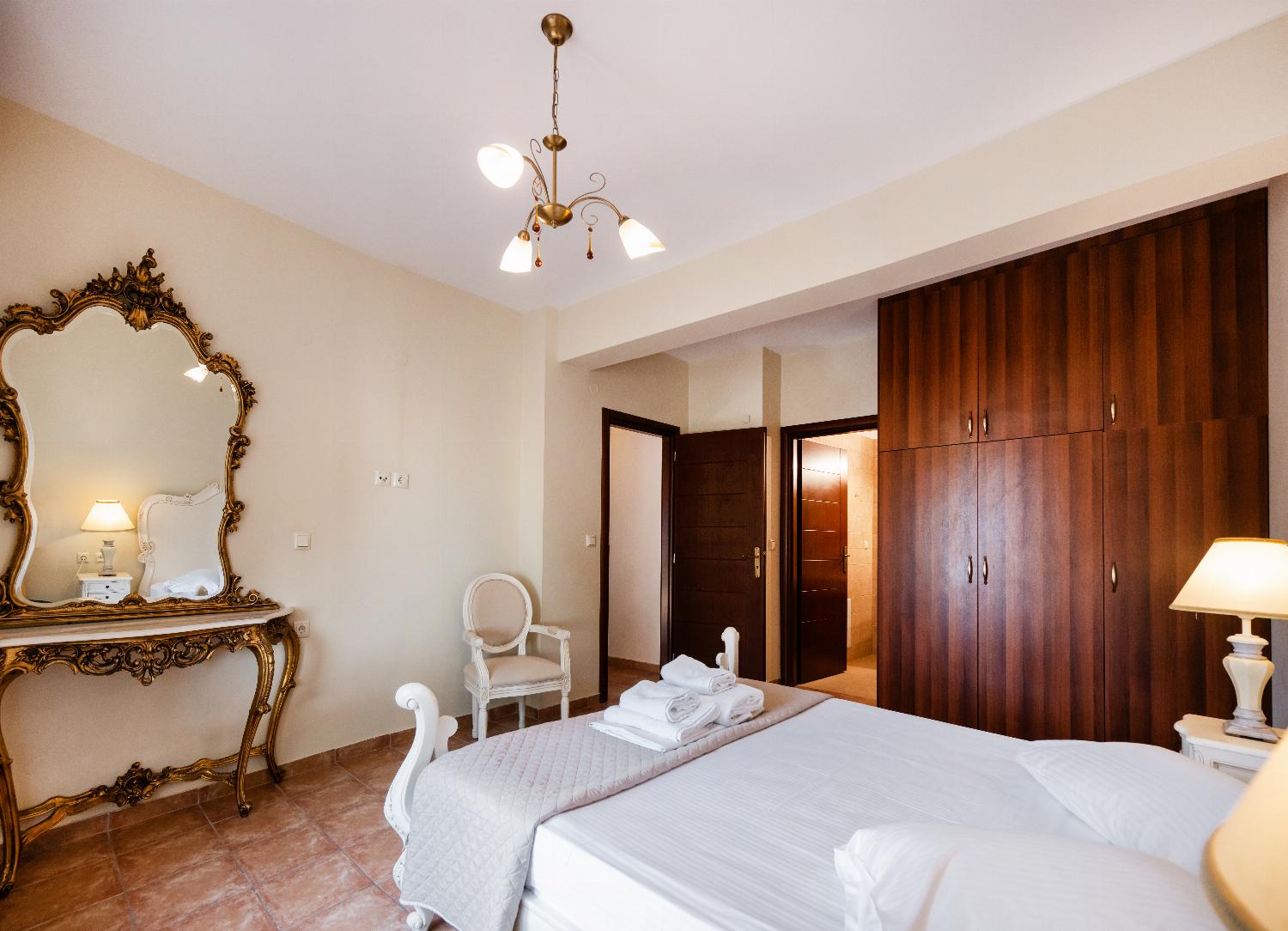 Villa bedroom with a large wood wardrobe and an ornate gold-framed vanity mirror.