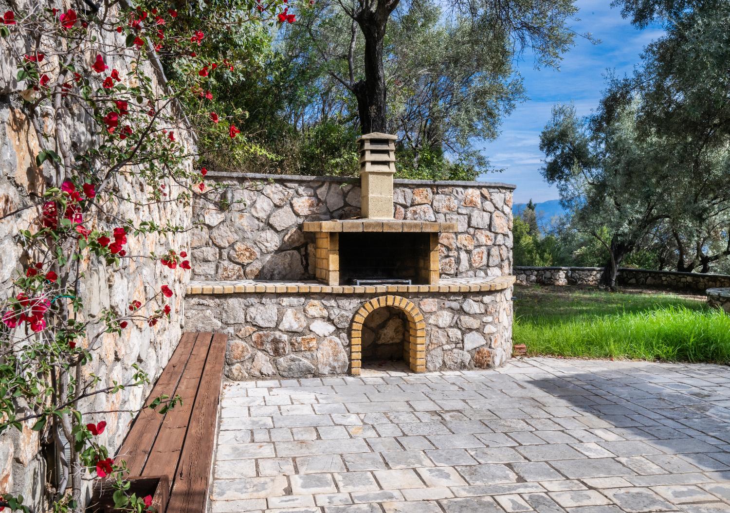 Built-in stone barbecue oven on a paved patio surrounded by green trees.