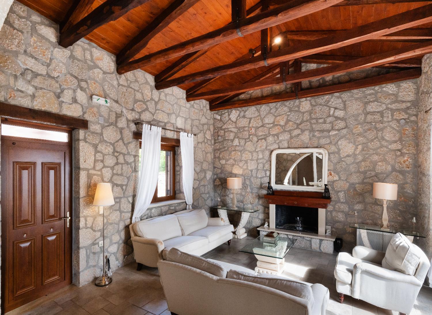 Cozy living room with stone walls, a fireplace, and a vaulted wooden roof.