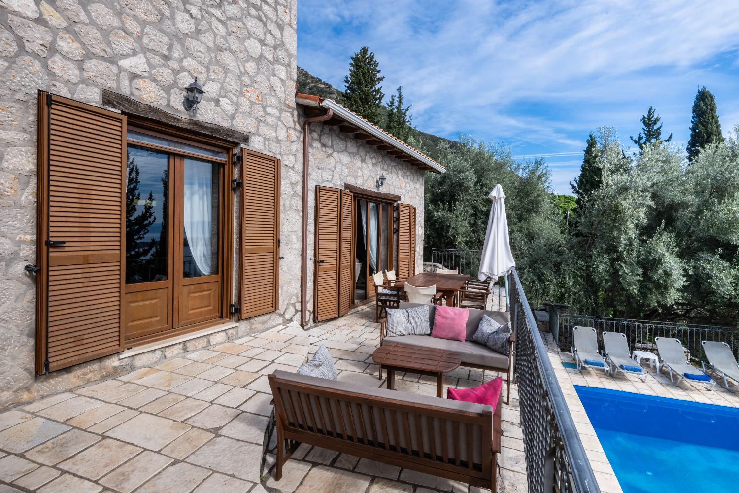 Stone villa terrace with outdoor lounge sofas, dining set, and pool view.