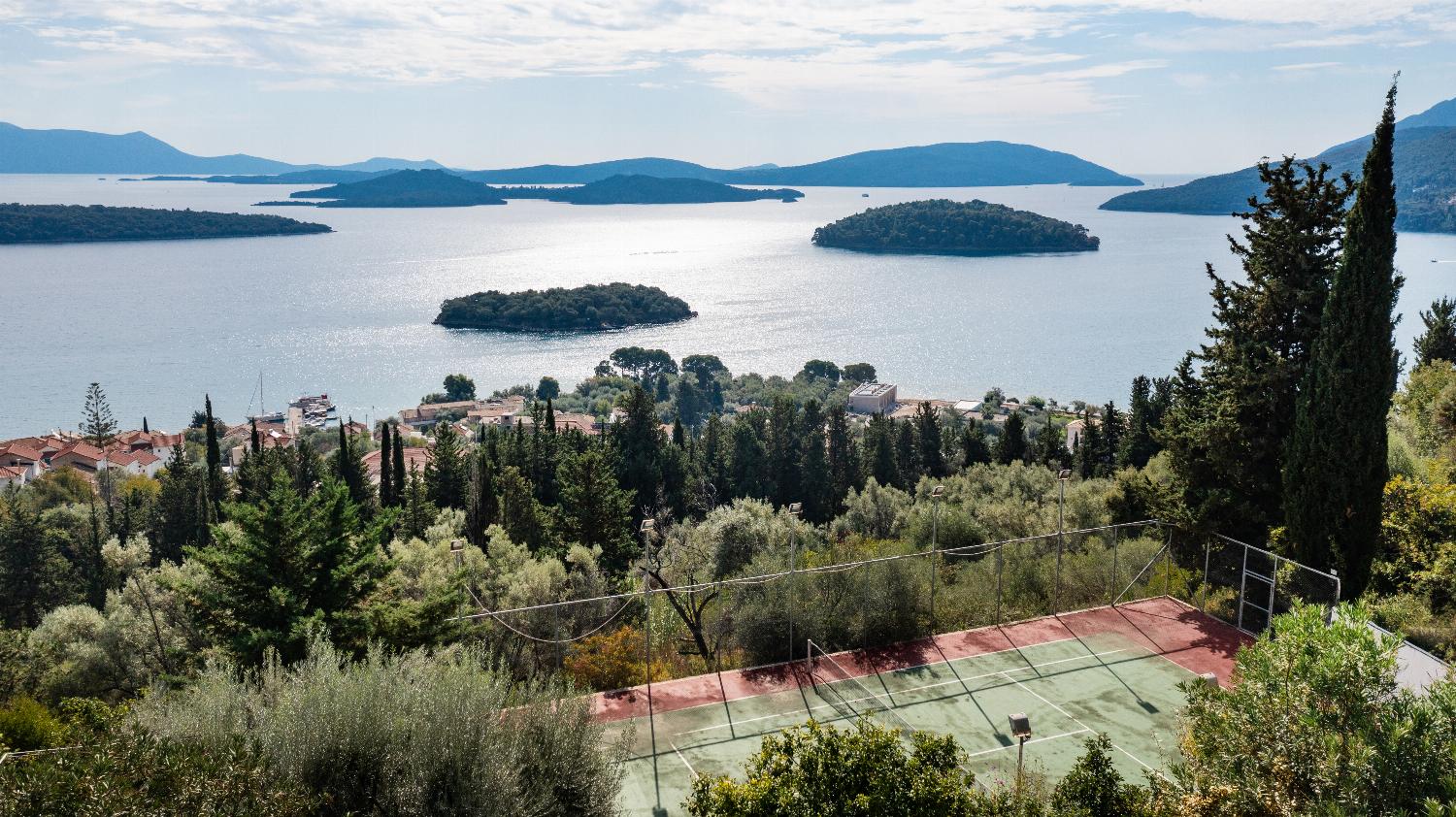 Private outdoor tennis court overlooking a panoramic sea bay with scattered green islands.