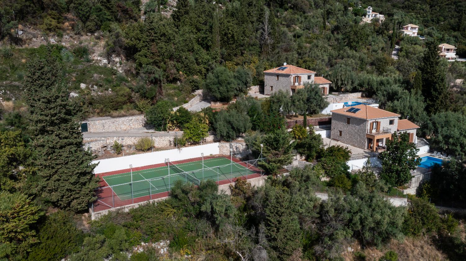 Aerial view of a hillside villa complex featuring stone houses, private pools, and a tennis court.