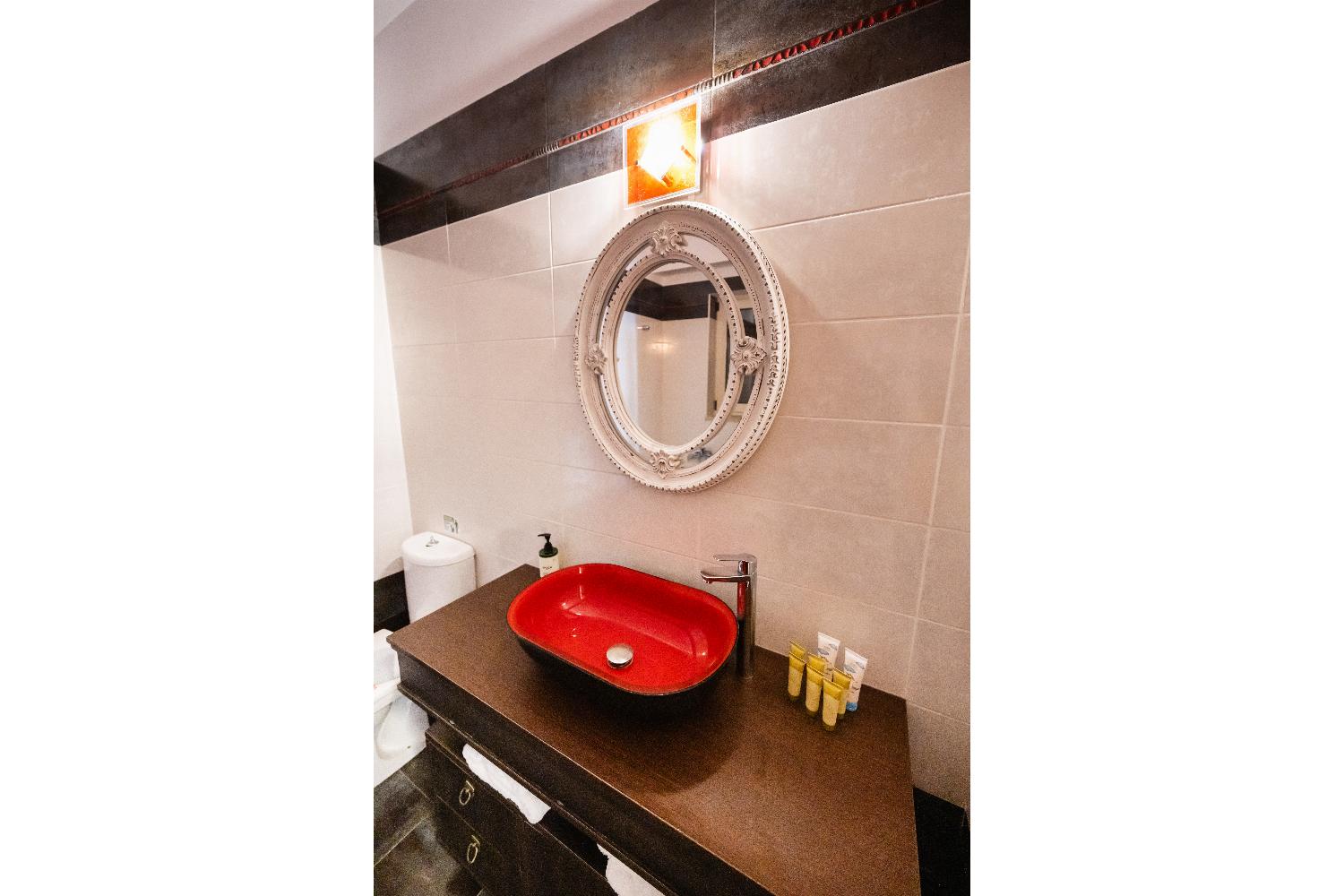 Modern vanity area featuring a vibrant red vessel sink and an ornate oval mirror.