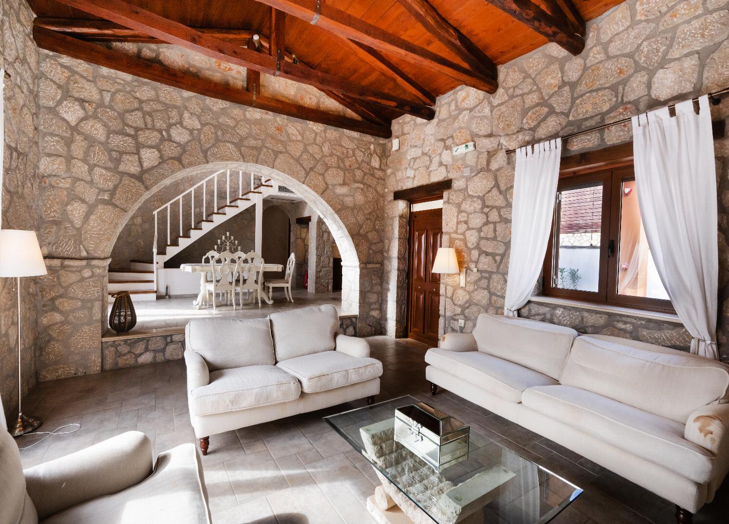 Stone living room with cream sofas, high timber ceilings, and an arched dining entryway.