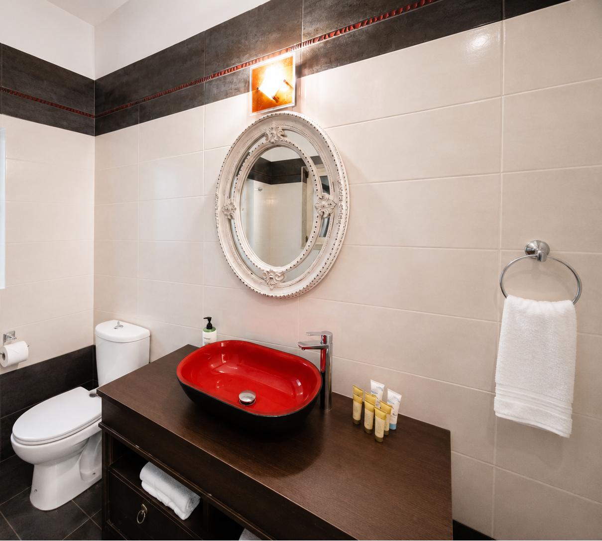 Modern vanity area featuring a vibrant red vessel sink and an ornate oval mirror.