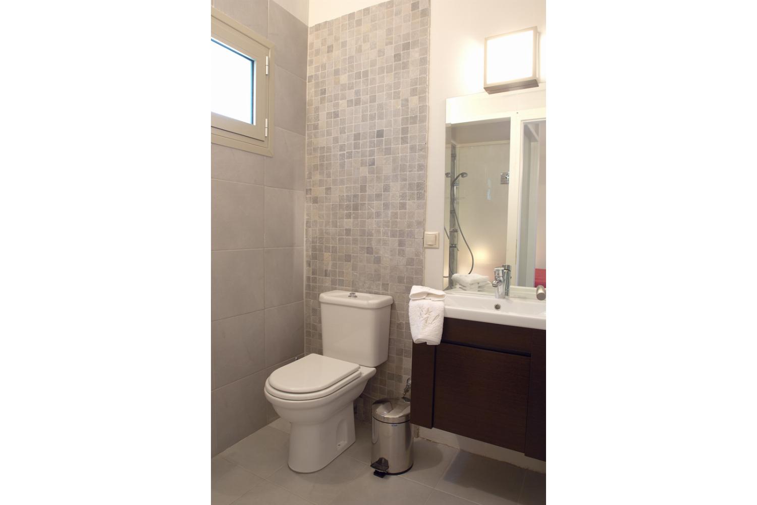 A modern bathroom features a compact dark vanity sink paired with a large mirror, neutral mosaic tiling, and clean white towels hanging nearby.