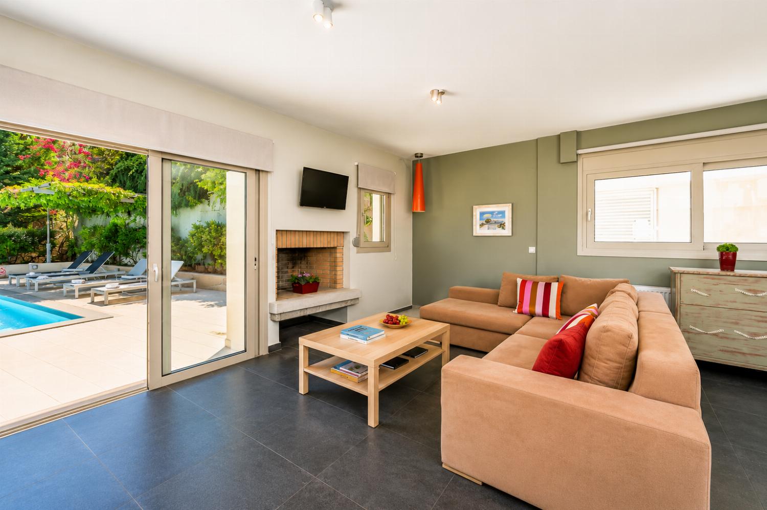 A cozy living area features a beige sectional sofa facing a fireplace and a wall-mounted television, with large sliding glass doors opening directly onto the outdoor pool patio.
