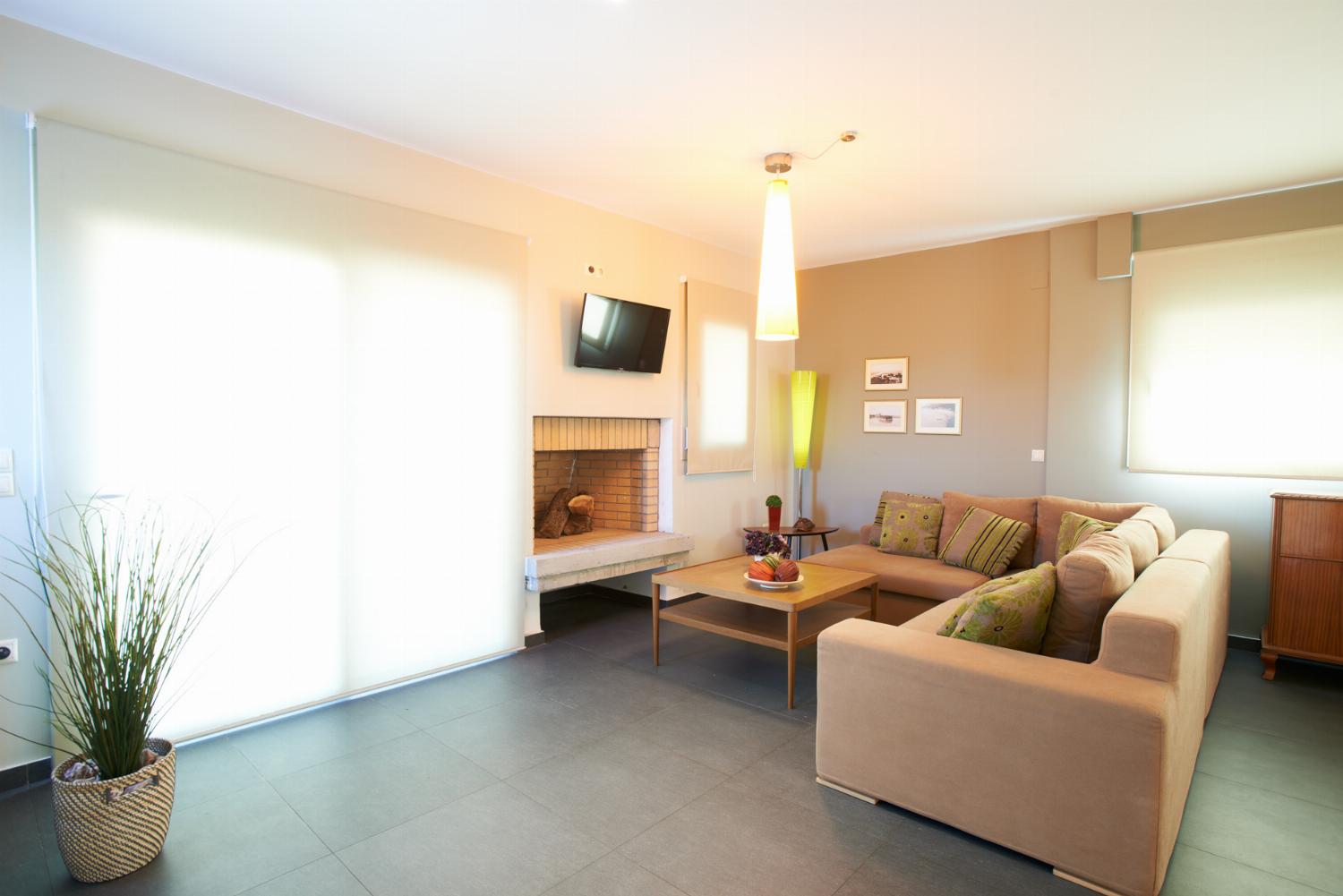 A cozy living area features a beige sectional sofa facing a fireplace and a wall-mounted television, with large sliding glass doors opening directly onto the outdoor pool patio.
